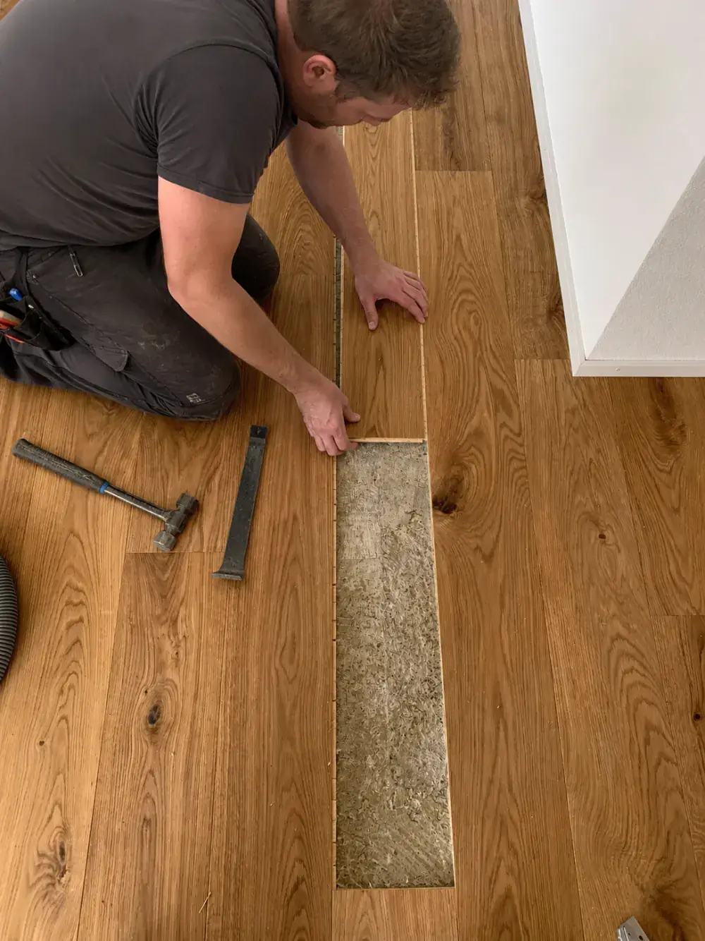 Handwerker tauscht mit Hammer und Stemmeisen eine beschädigte Parkettdiele aus, darunter ist der Unterboden sichtbar