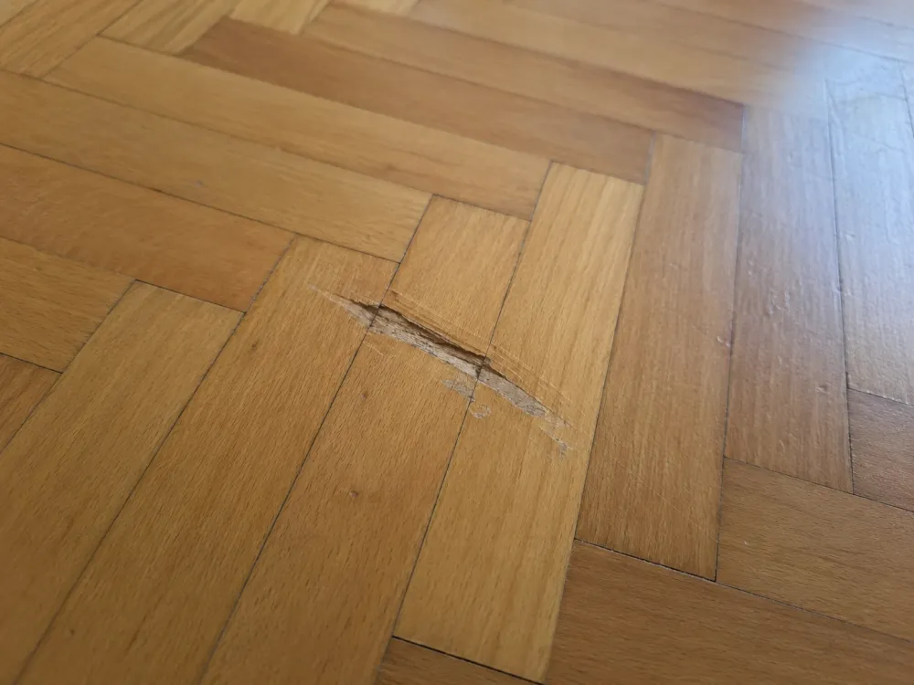 Parkettboden mit gesplitterter, beschädigter Stelle vor der Reparatur